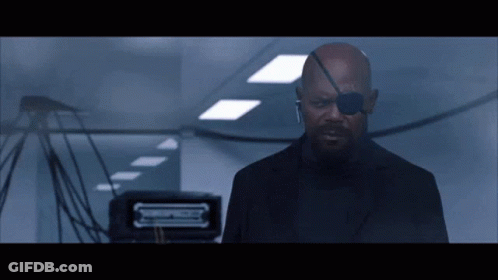 Man In Black Suit With Eye Patch In Hallway GIF
