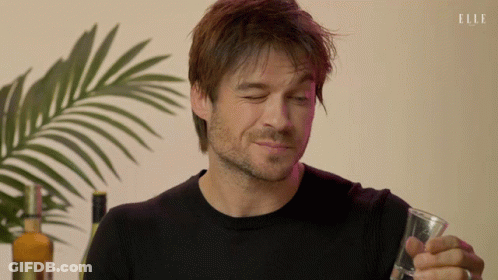 Man In Black Sweater Holds Glass, Bottle Of Elle, Palm Tree GIF