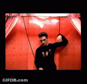 Man In Black Sweater In Front Of Red Wall GIF