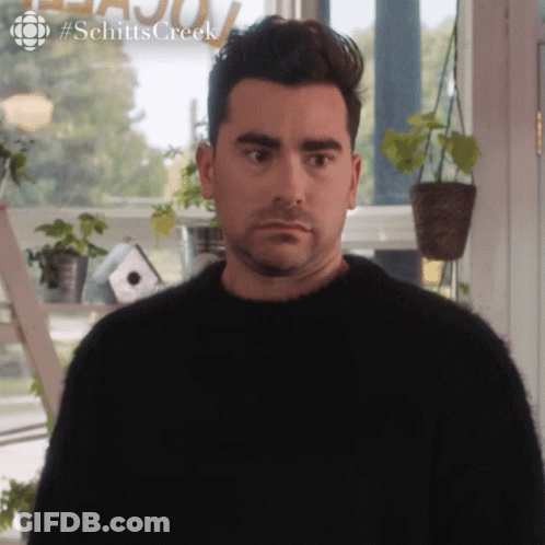Man In Black Sweater In Front Of Schitts Creek Sign GIF