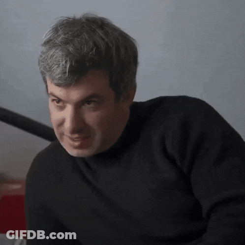 Man In Black Sweater Looks At Camera GIF