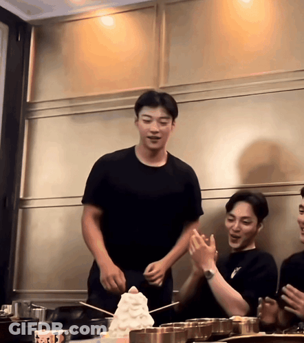 Man In Black T-Shirt Standing In Front Of Ice Cream Stack GIF