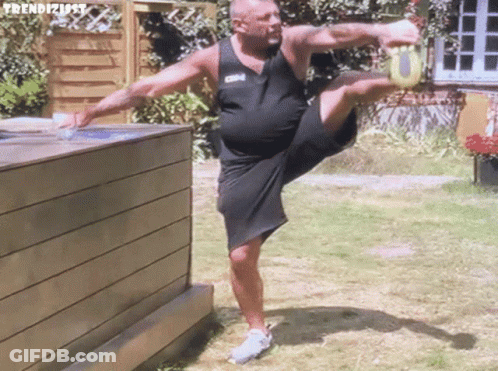 Man In Black Tank Top And Shorts Doing Leg Stretch GIF