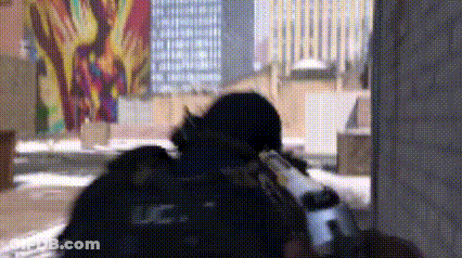 Man In Black Uniform Holding Gun In Front Of Graffiti Building GIF
