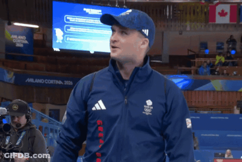 Man In Blue Adidas Jacket In Front Of Milano Cortina Screen GIF