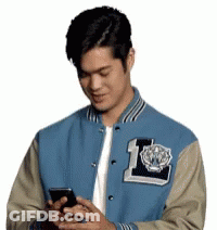 Man In Blue And Tan Varsity Jacket Looking At Cell Phone GIF