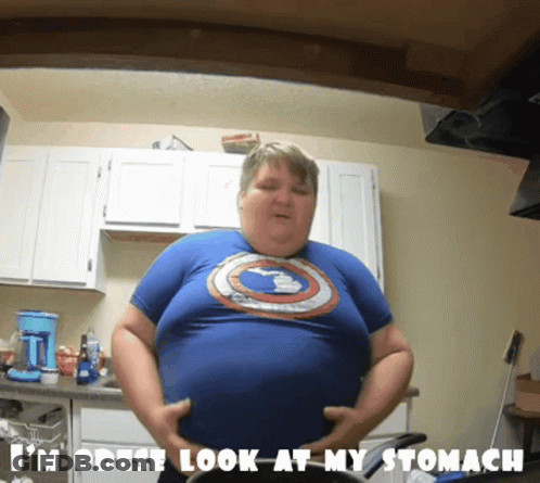 Man In Blue Captain America Shirt Holding Belly In Kitchen GIF