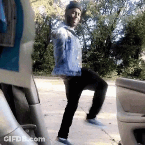 Man In Blue Denim Jacket Standing On One Leg In Front Of Car GIF