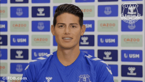 Man In Blue Everton Shirt Smiling In Front Of Everton Logos GIF