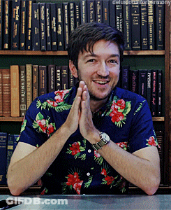 Man In Blue Floral Shirt Smiling At Bookshelf GIF