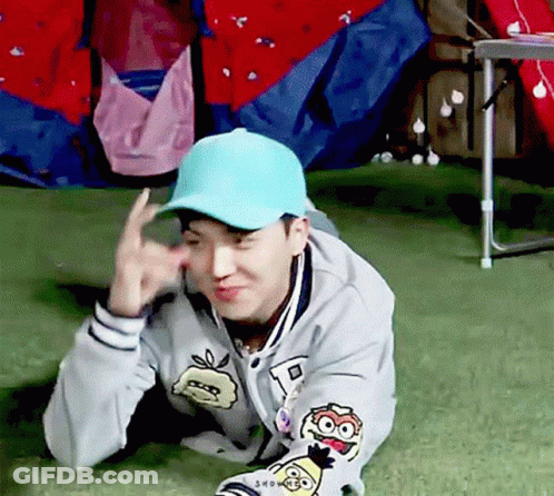 Man In Blue Hat And Gray Jacket Laying On Grass Making Funny Face GIF