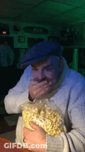 Man In Blue Hat Holding Popcorn Covering Mouth GIF