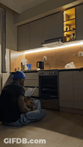 Man In Blue Hat Reading Book In Kitchen GIF