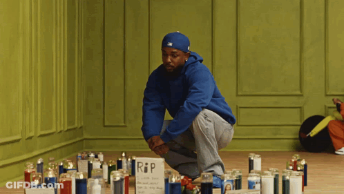 Man In Blue Hoodie Kneeling By Candles RIP Sign GIF