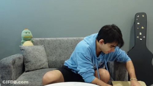 Man In Blue Hoodie Sitting On Couch With Guitar Case GIF