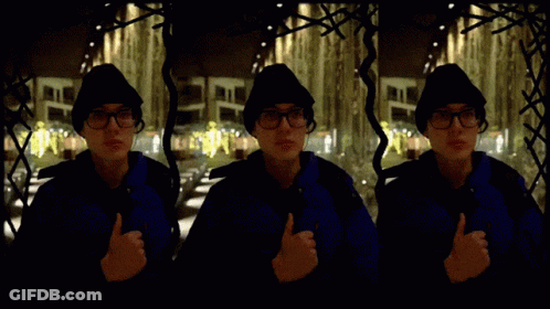 Man In Blue Jacket Giving Thumbs Up In Front Of Building GIF