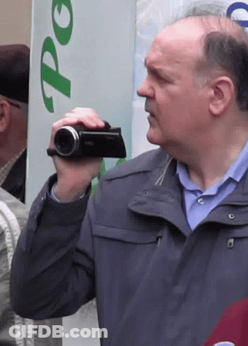 Man In Blue Jacket Holding Camera Near Po Sign GIF