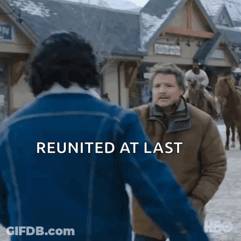 Man In Blue Jacket Talking To Man In Brown Jacket In Snowy Town GIF