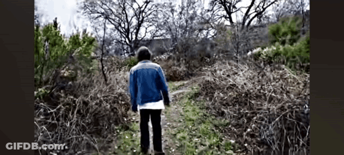 Man In Blue Jacket Walking Down Dirt Path In Woods GIF