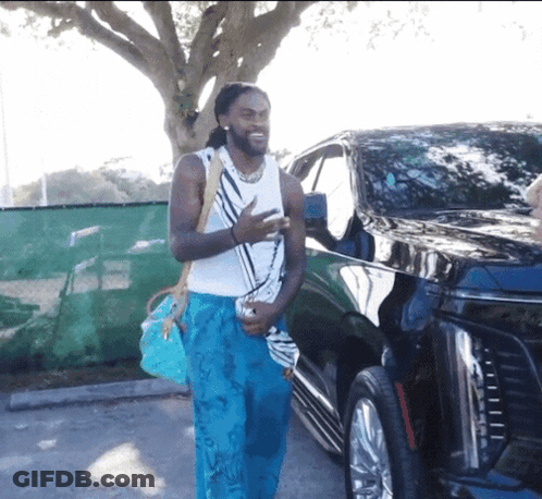 Man In Blue Pants And White Tank Top Standing By Black Car GIF