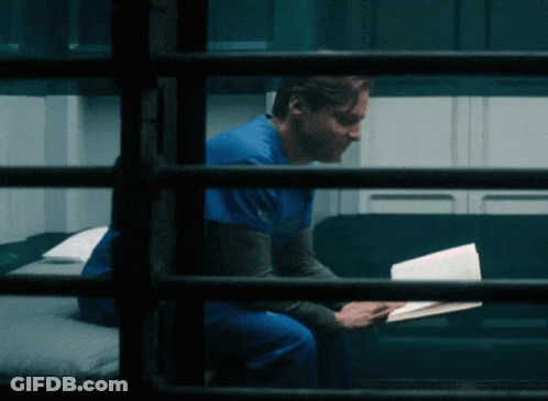 Man In Blue Scrub Top Reading Book On Couch GIF