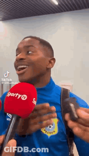 Man In Blue Shirt And Backpack Talking Into Microphone GIF