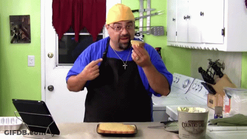 Man In Blue Shirt And Black Apron Holding Cornbread GIF