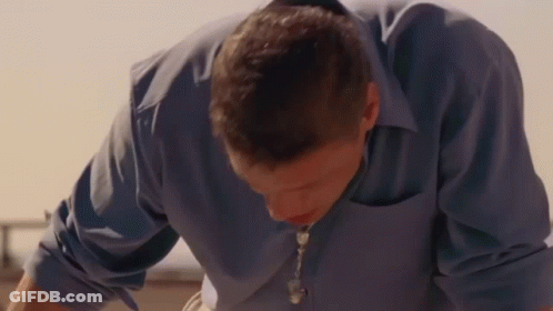 Man In Blue Shirt And Necklace Looking Down GIF