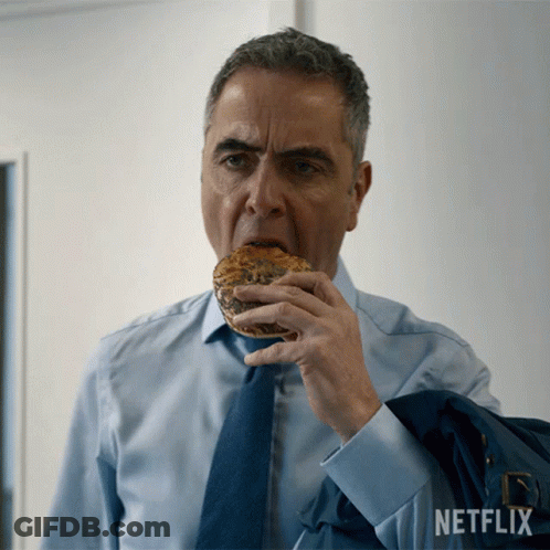 Man In Blue Shirt And Tie Eating Bagel With Netflix Logo GIF