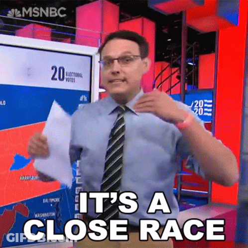 Man In Blue Shirt And Tie Holding Paper Saying It's A Close Race GIF