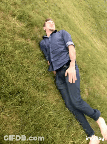 Man In Blue Shirt And Tie Laying On Grassy Hill GIF