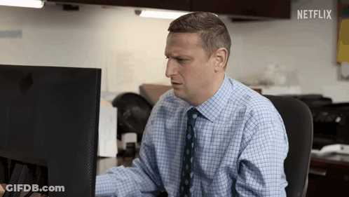 Man In Blue Shirt And Tie Sitting In Front Of Netflix Sign GIF