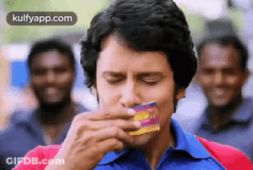 Man In Blue Shirt Eating Candy Bar While Men Laugh GIF