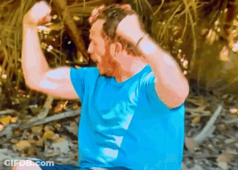 Man In Blue Shirt Flexing Muscles Sitting On Ground GIF