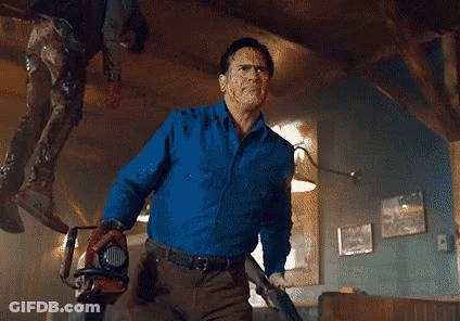 Man In Blue Shirt Holding Chainsaw And Gun GIF