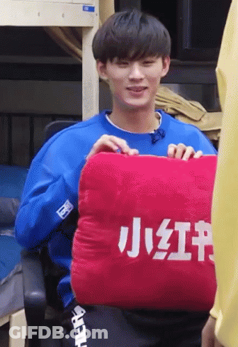 Man In Blue Shirt Holding Red Pillow With Chinese Characters GIF
