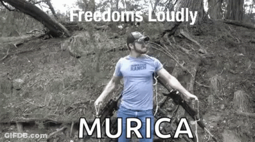 Man In Blue Shirt Holding Two Guns In Woods GIF