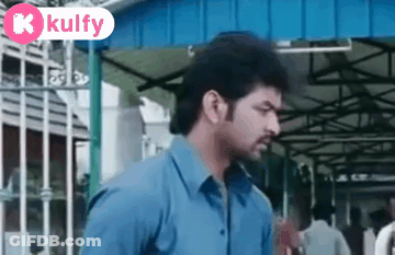 Man In Blue Shirt In Front Of Building With Kulfy Sign GIF