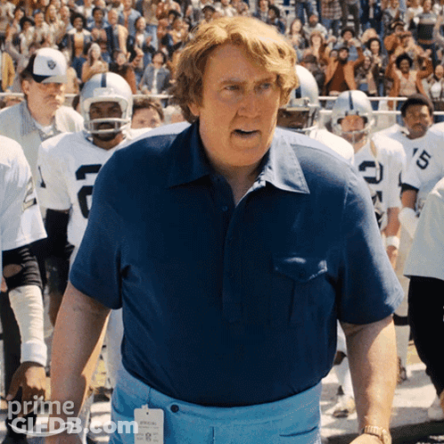 Man In Blue Shirt In Front Of Football Players With Letter C GIF