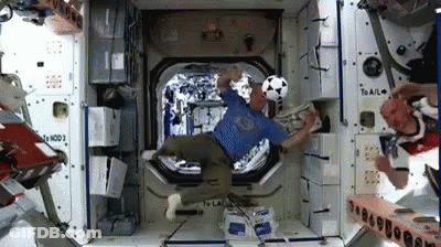 Man In Blue Shirt Kicking Soccer Ball In Space Station GIF