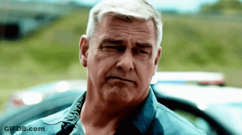 Man In Blue Shirt Looking At Camera By Police Car GIF