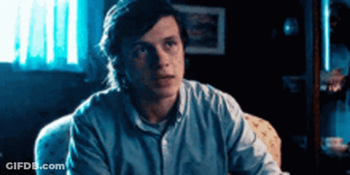 Man In Blue Shirt Looking At Camera In Dark Room GIF