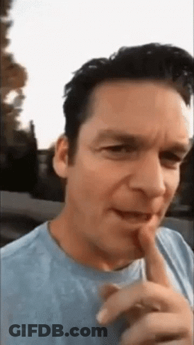 Man In Blue Shirt Making Funny Face With Finger On Lips GIF