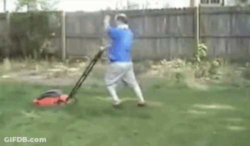 Man In Blue Shirt Mowing Lawn With Red Lawn Mower GIF