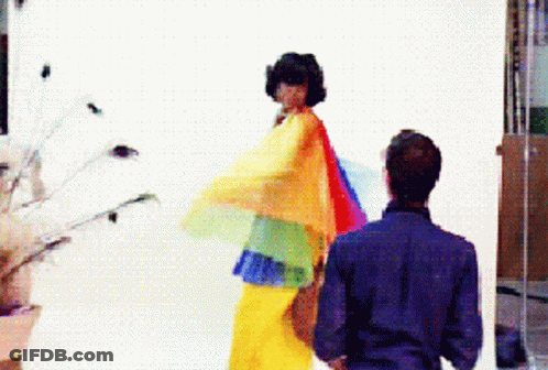 Man In Blue Shirt Next To Woman In Rainbow Dress GIF