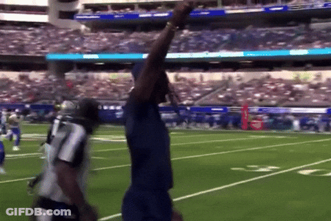 Man In Blue Shirt On Football Field With Arm Up GIF