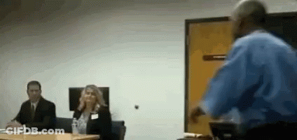 Man In Blue Shirt Presenting To Group At Table GIF