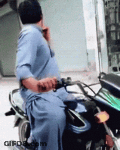 Man In Blue Shirt Riding Motorcycle Talking On Cell Phone GIF