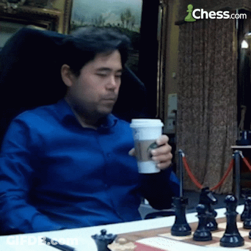 Man In Blue Shirt Sitting At Chess Board With Coffee GIF