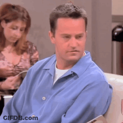 Man In Blue Shirt Sitting In Waiting Room With Woman Reading Book GIF